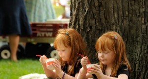 Twins little girls eat ice cream at festival