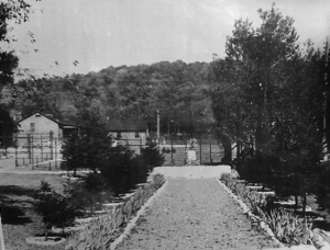 Photo showing the entrance to the POW camp as well as the CCC fountain in the background. To the left is the gate to the main POW compound. The POW mess hall is in the rear. Copied by Chris Champion via the Cumberland County Historical Society.