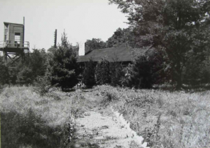 A photo showing one of the guard towers and a pathway leading to a log cabin used to house the office and quarters of the camp's commander, Major Lawrence Thomas. Photo from the Pine Grove Furnace Park Office via the Cumberland County Historical Society.