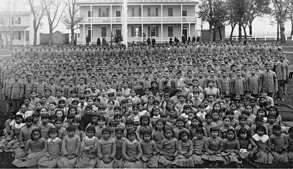 black and white photo of hundreds of school students sitting in rows in front a school building