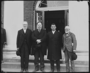"Robert C. Ogden, U.S. Secretary of War William Howard Taft, Booker T. Washington and Andrew Carnegie, standing on the steps of a building, at the Tuskegee Institute's 25th anniversary celebration"