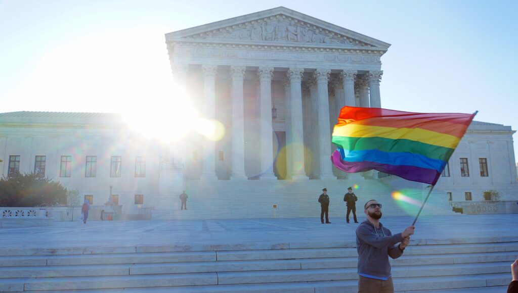 Man holds rainbow flag outside of the supreme court building on 4/28/2015