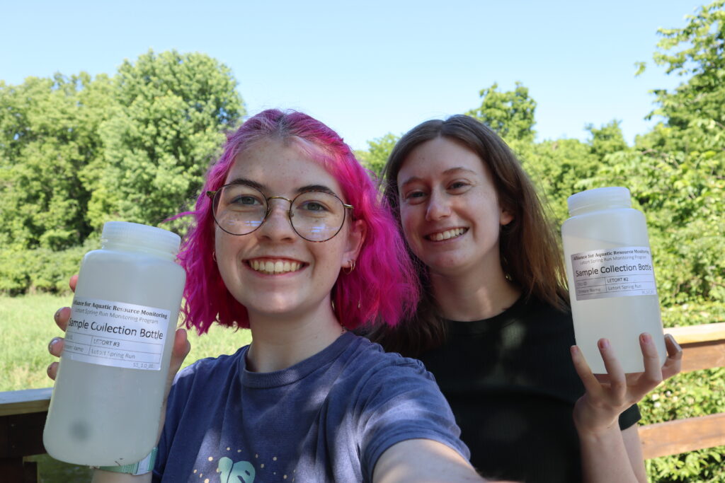 Photo shows watershed coordinators Grace and Kyra holding sample collection bottles while LeTort monitoring.