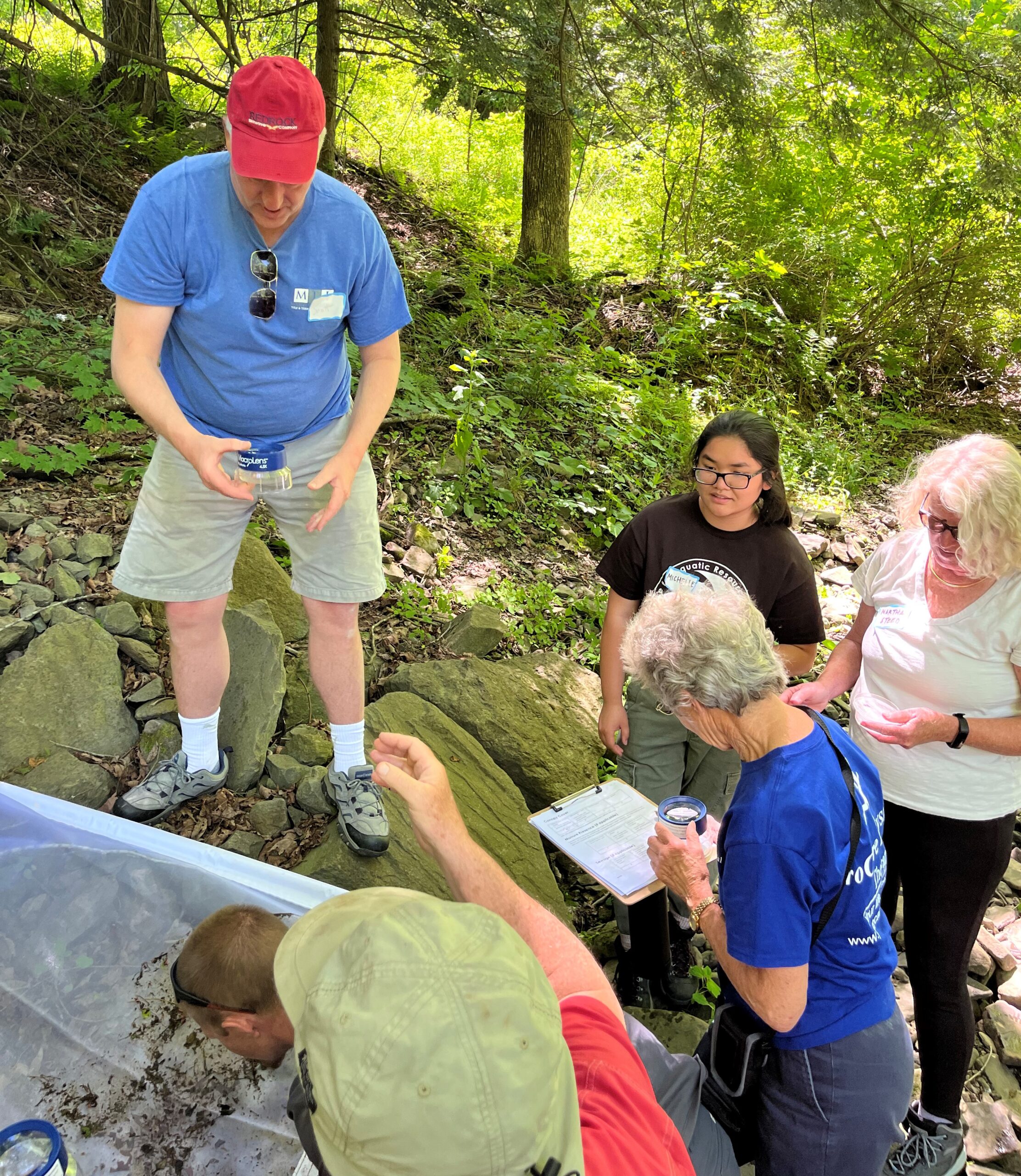 Image shows author and volunteers sorting through macroinvertebrates along the banks of a stream.