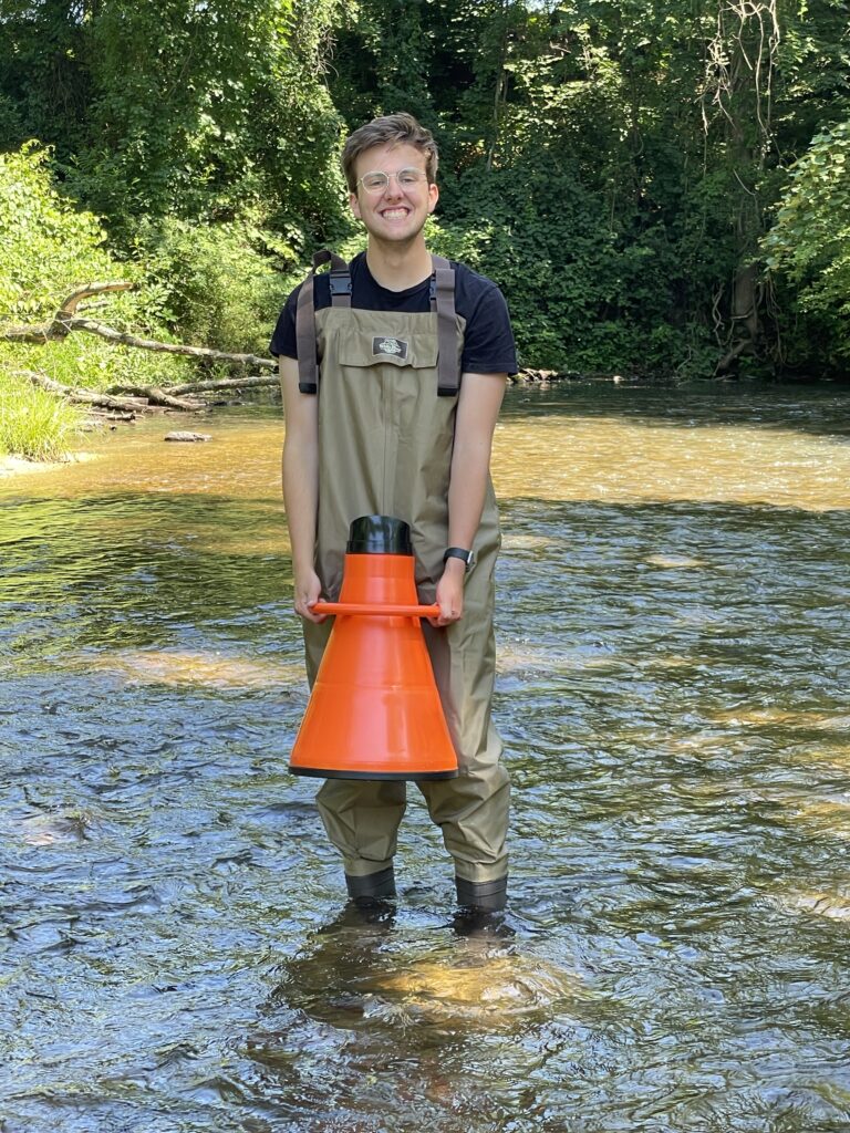 Nick standing in a stream holding a stream viewer, allowing him to look into the water unobstructed.