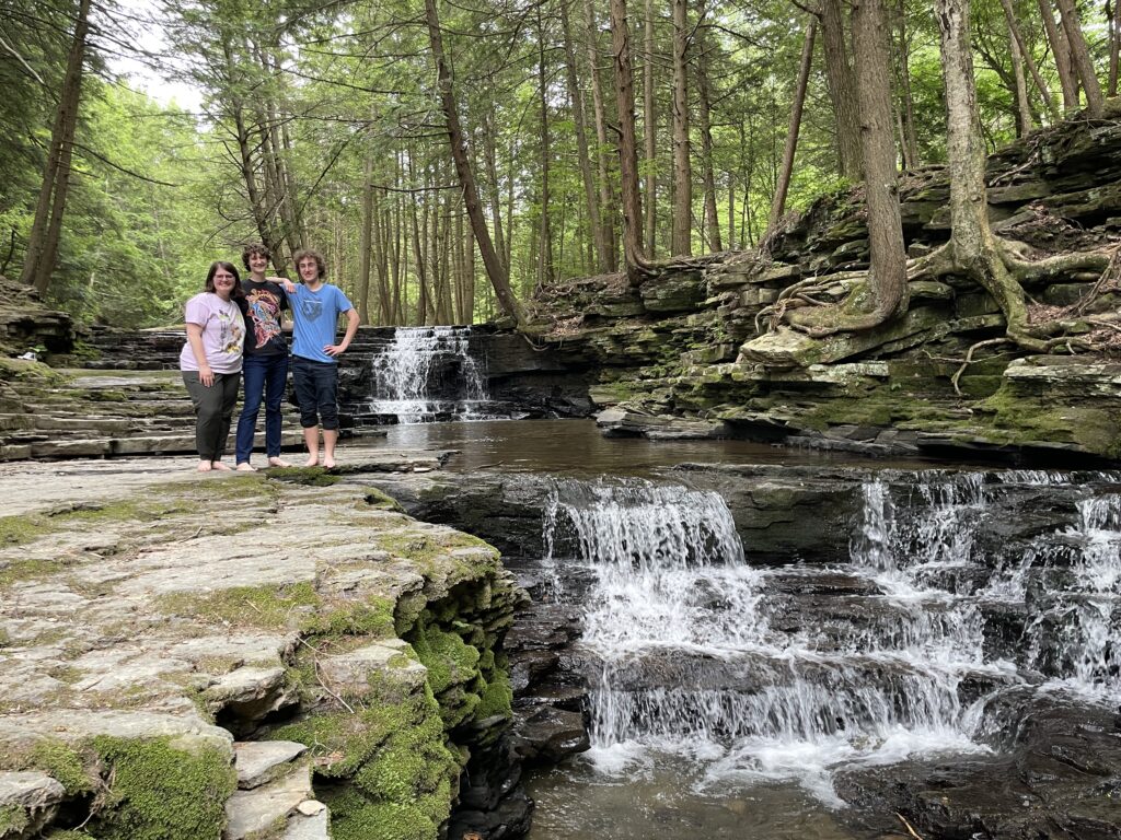 Crosby stands with two other staff members beside a waterfall at Salt Springs State Park