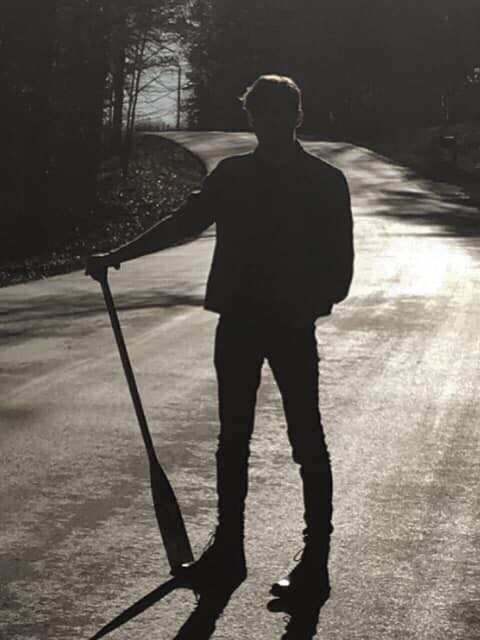 Silhouette of Eli holding an oar on a sunlit road