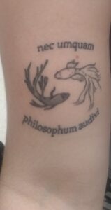 A tattoo on my right arm: one black beta fish and one white beta fish circling each other to form a yin yang symbol with the quote nec umquam philosophum audivi (“I never listened to a philosopher,” Petronius, Satyrica 71.12).