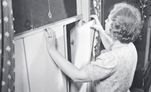 Woman installs boards in her windows to block light during a blackout drill